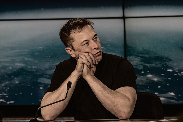 Photo by Capitalist Money on June 16, 2024. May be an image of Elon Musk sits with his hands together in front of him, against a backdrop that appears to show the ocean. .