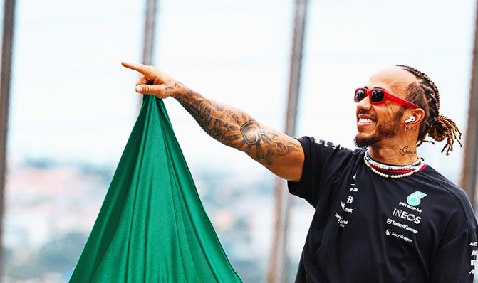 Photo by Capitalist Money on June 16, 2024. May be an image of Lewis Hamilton, a British Formula One driver, smiling and waving a green flag. The image may contain text such as 'INEOS', 'TeamViewer', 'Snapdragon', 'PETRONAS'.