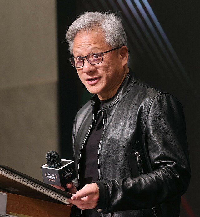 Photo by Capitalist Money on June 06, 2024. May be an image of A man with grey hair wearing glasses and a black leather jacket speaks into a microphone. He appears to be on a stage or at a podium. .