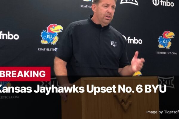 Photo by Capitalist Money on November 17, 2024. May be an image of A man in a black KU Jayhawks shirt is giving a press conference. The background features KU logos and sponsors. The text on the image reads "BREAKING Kansas Jayhawks Upset No. 6 BYU." The image may contain text such as 'KUATHL', '①fnbo', 'KU', 'fnbo', 'KU', 'KUATHLETI', 'fnbo', 'KU', 'KUATHLETICS.COM', 'BREAKING', 'Kansas Jayhawks Upset No. 6 BYU', 'KUATHLETICS.COM', 'COM', 'Image by Tigersofhighland70'.