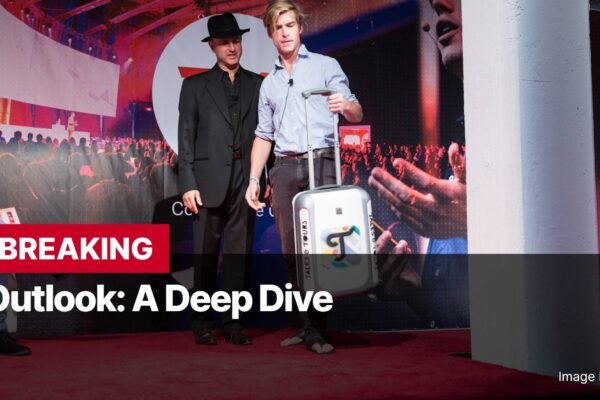 Photo by Capitalist Money on November 26, 2024. May be an image of Two men stand on a stage, one holding a suitcase. The background shows a large screen with an audience and the text 'Outlook: A Deep Dive'. The image has a 'Breaking' banner at the bottom. The image may contain text such as 'BREAKING', 'Outlook: A Deep Dive', 'Image by 1Veertje', 'SALES & TOURS', 'SALES & TOURS'.